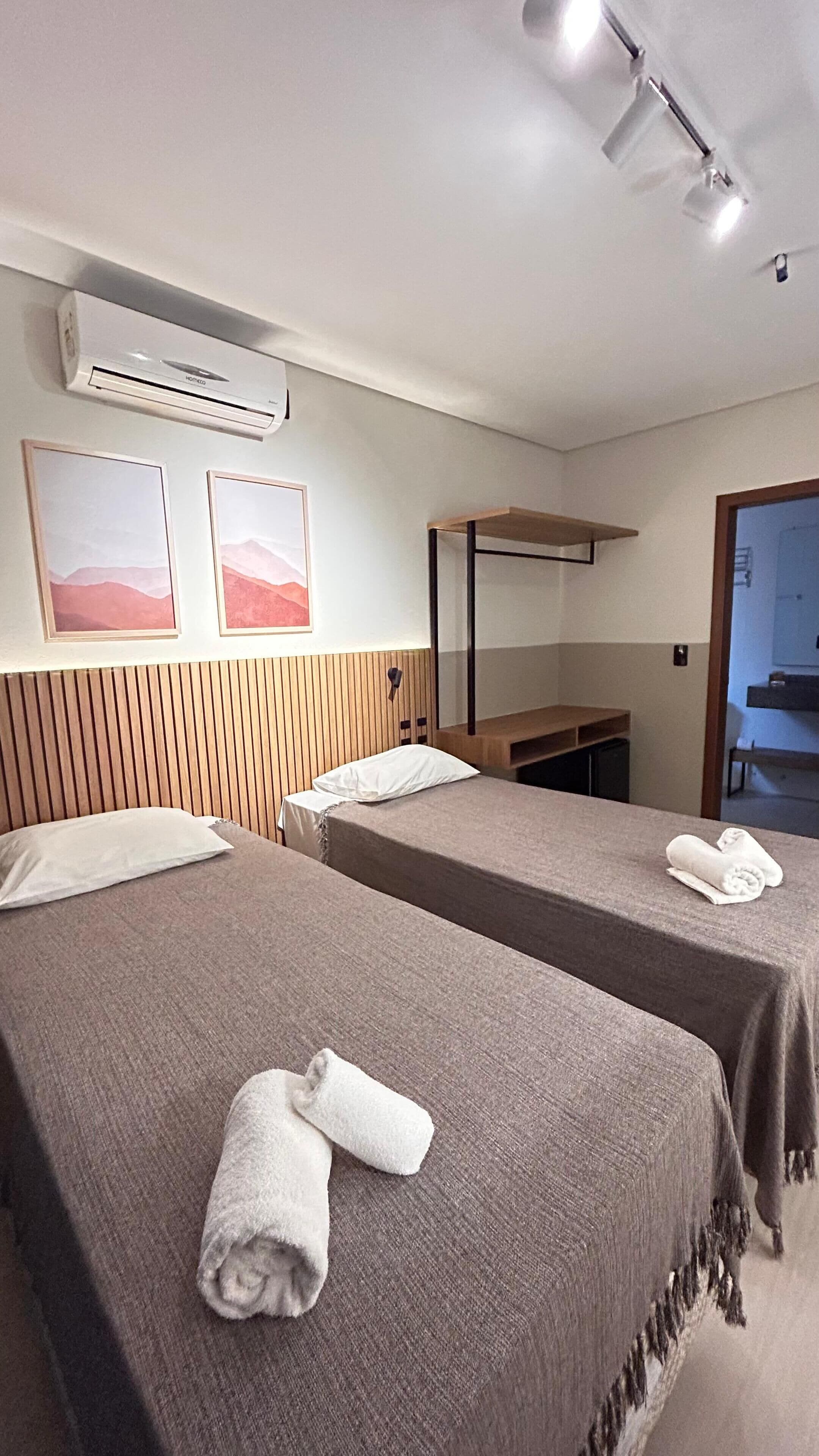 Habitación de hotel con dos camas, cabecero de madera, unidad de aire acondicionado y un banco.