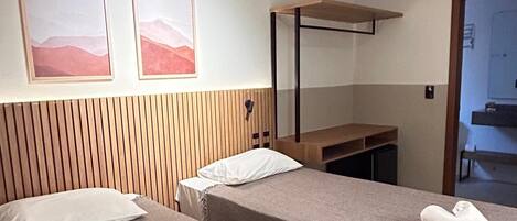 Habitación de hotel con dos camas, cabecero de madera, unidad de aire acondicionado y un banco.