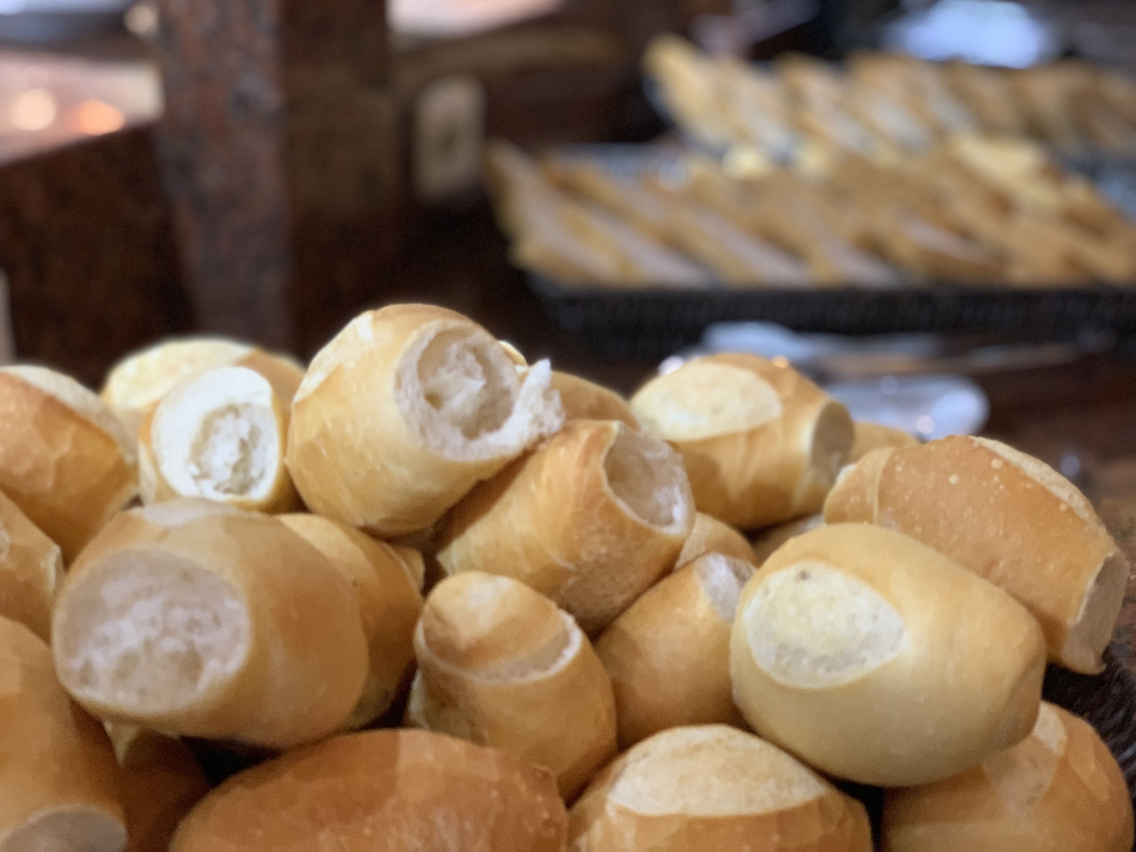 Ein Stapel runder, goldbrauner Brötchen mit sichtbarem, weichen Inneren, auf einer Holzoberfläche drapiert.