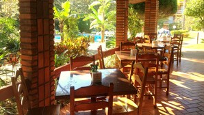 An outdoor patio area with brick pillars, wooden tables and chairs, and lush greenery in the background. - Hotel Sao Sebastiao Da Praia (Florianópolis)