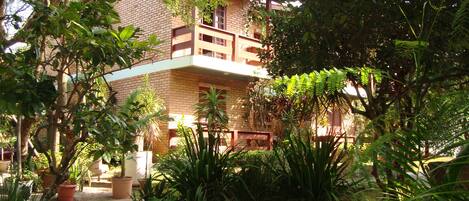 A two-story building with a balcony, surrounded by lush greenery and potted plants.