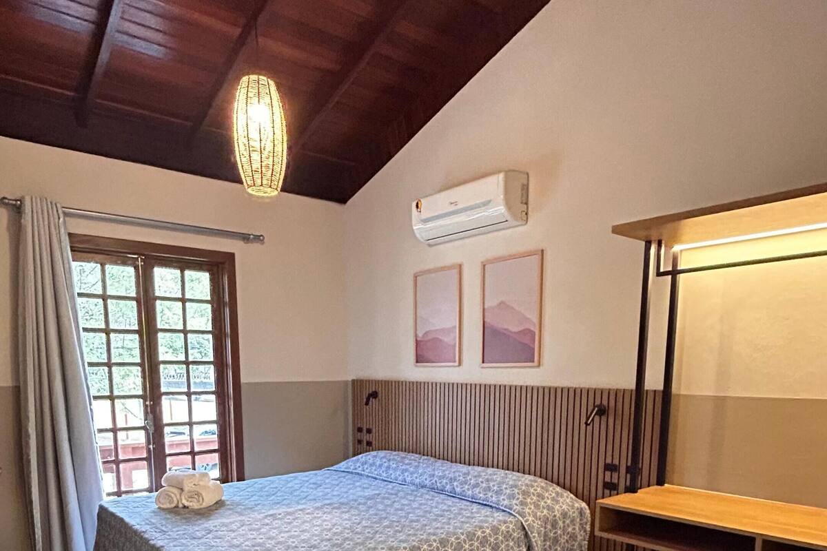 A bedroom with a bed, a desk, a window, and an air conditioning unit.
