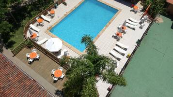 Vista aérea de una piscina con tumbonas y sombrillas, rodeada de una terraza de madera y una zona verde.