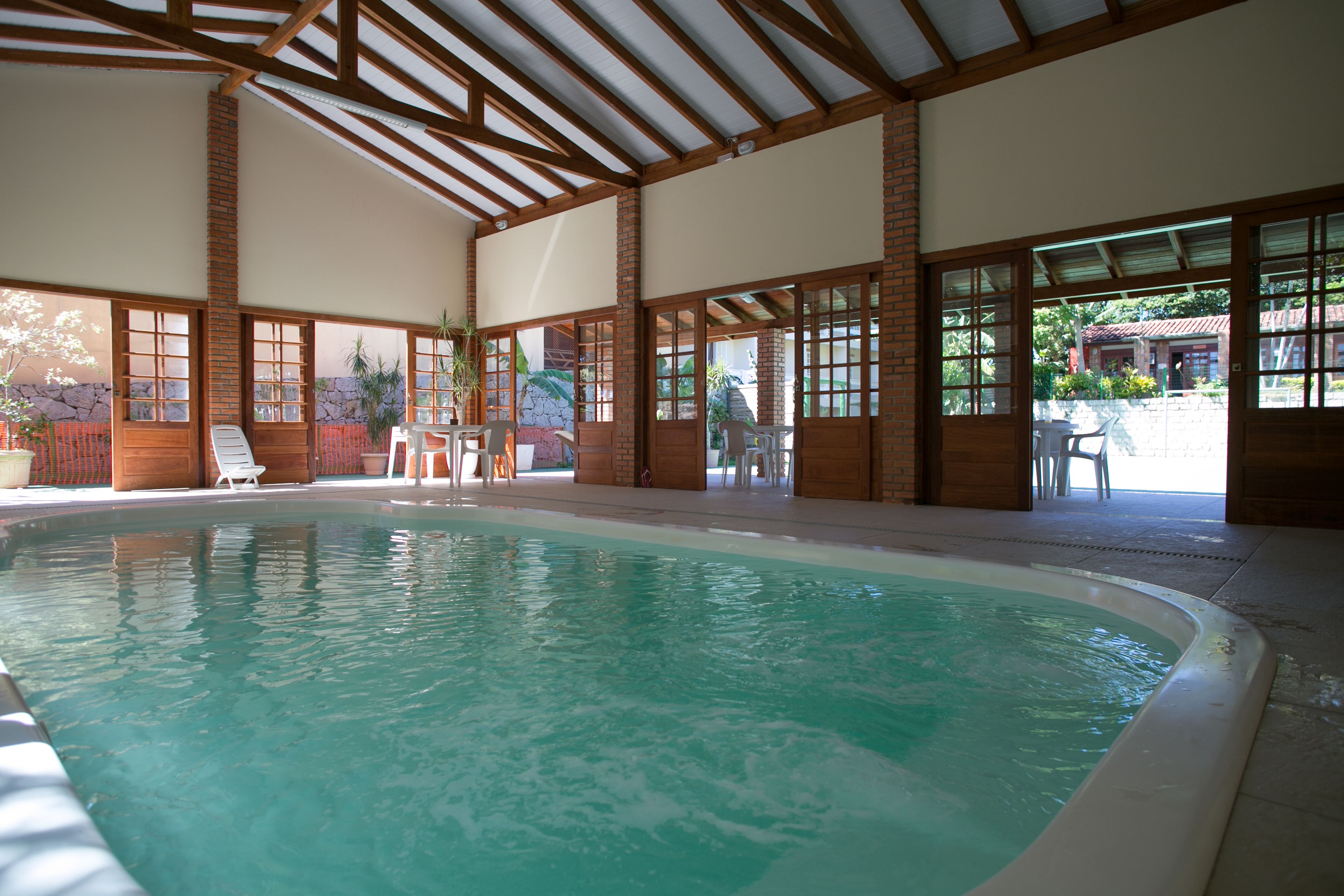An indoor swimming pool with clear water, wooden beams, and large windows.
