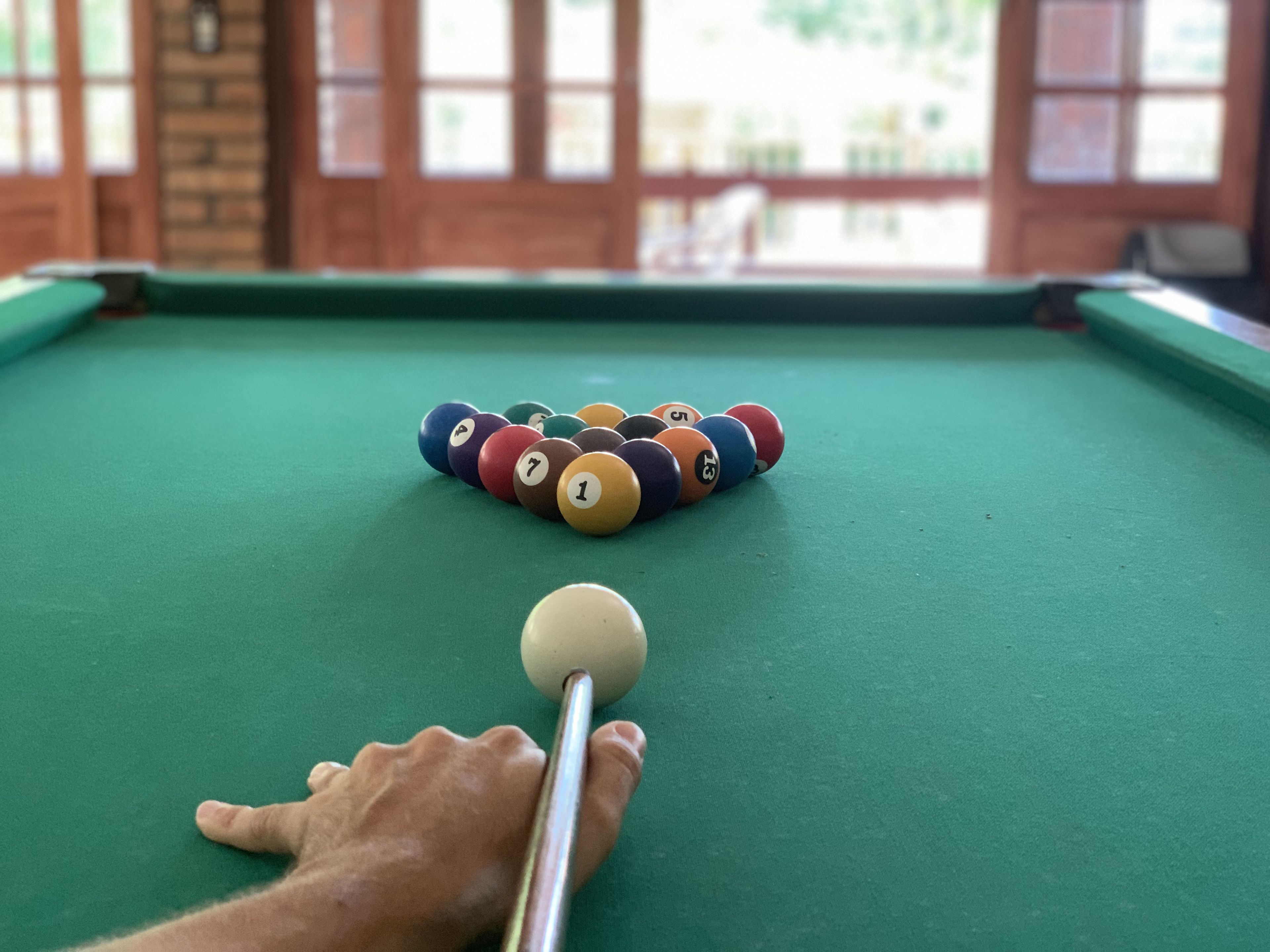 Una mesa de billar con bolas dispuestas en forma de triángulo, una bola blanca y un taco.