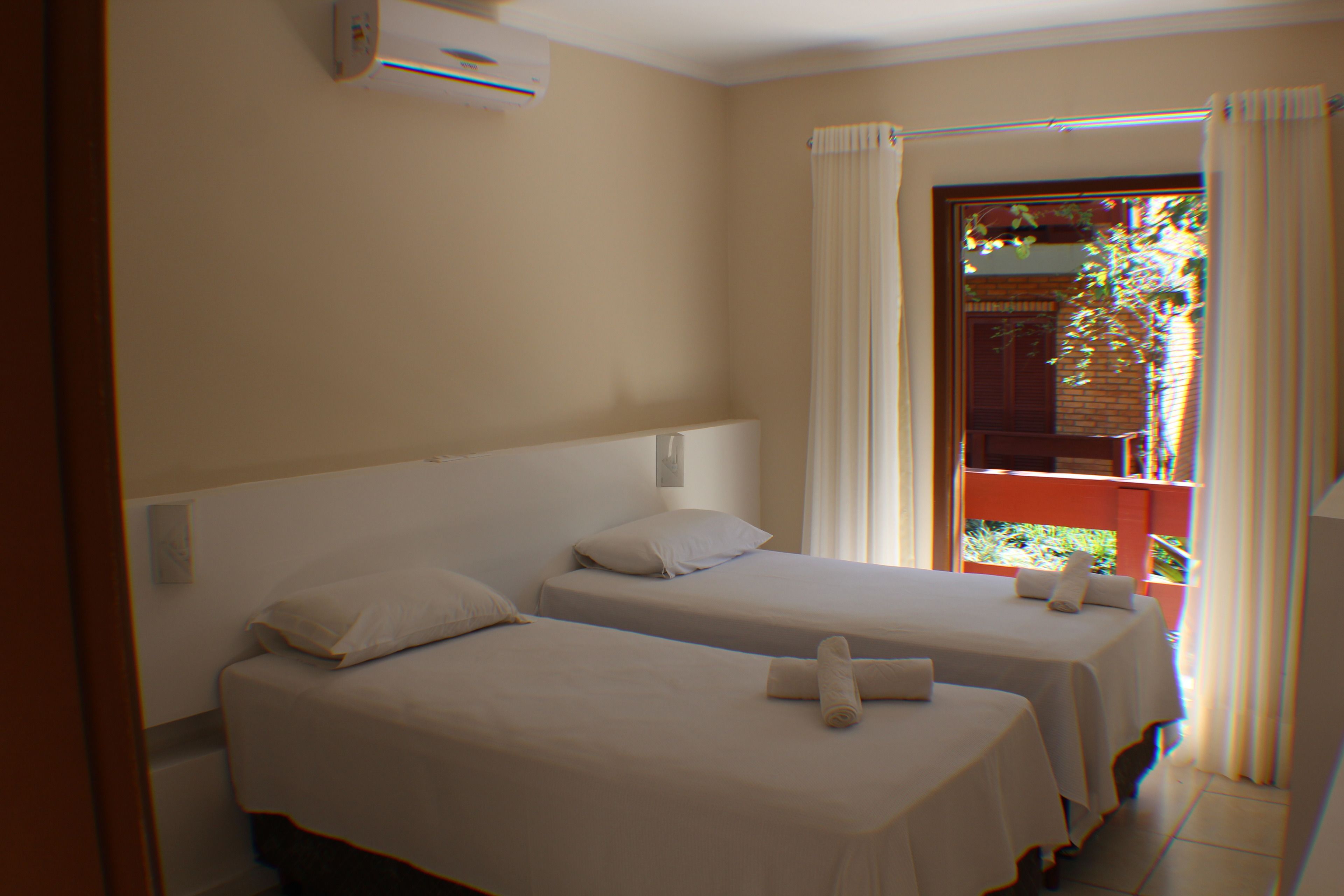 Une chambre d’hôtel avec deux lits simples, une fenêtre avec des rideaux et une vue sur la verdure.