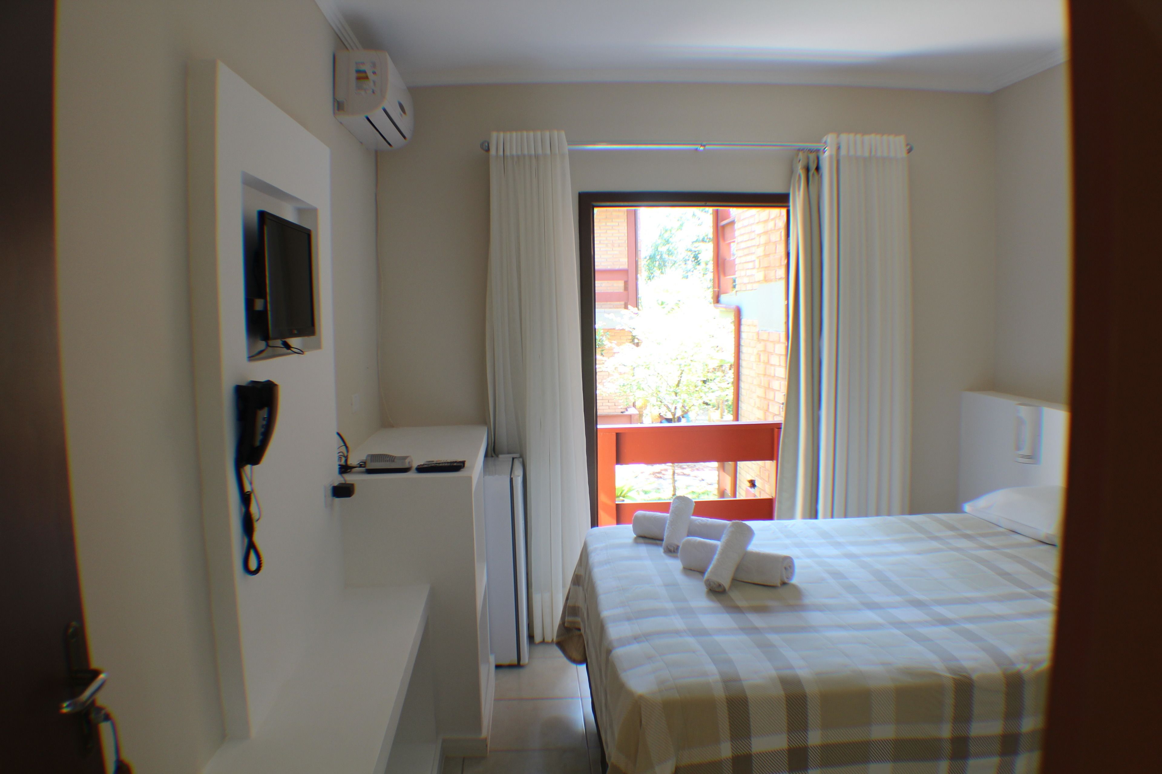 A hotel room with a bed, a TV mounted on the wall, and a window with curtains.