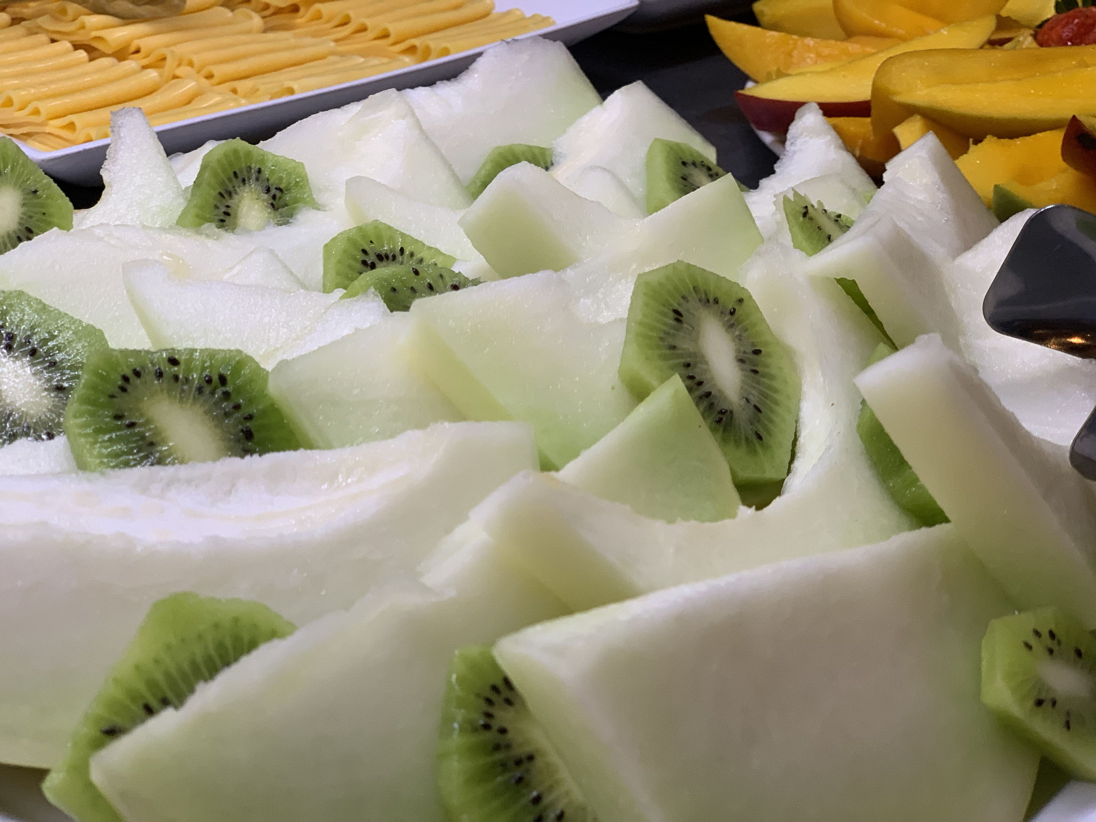 Uma variedade de frutas, incluindo fatias de kiwi e pedaços de melão, dispostas em uma bandeja.