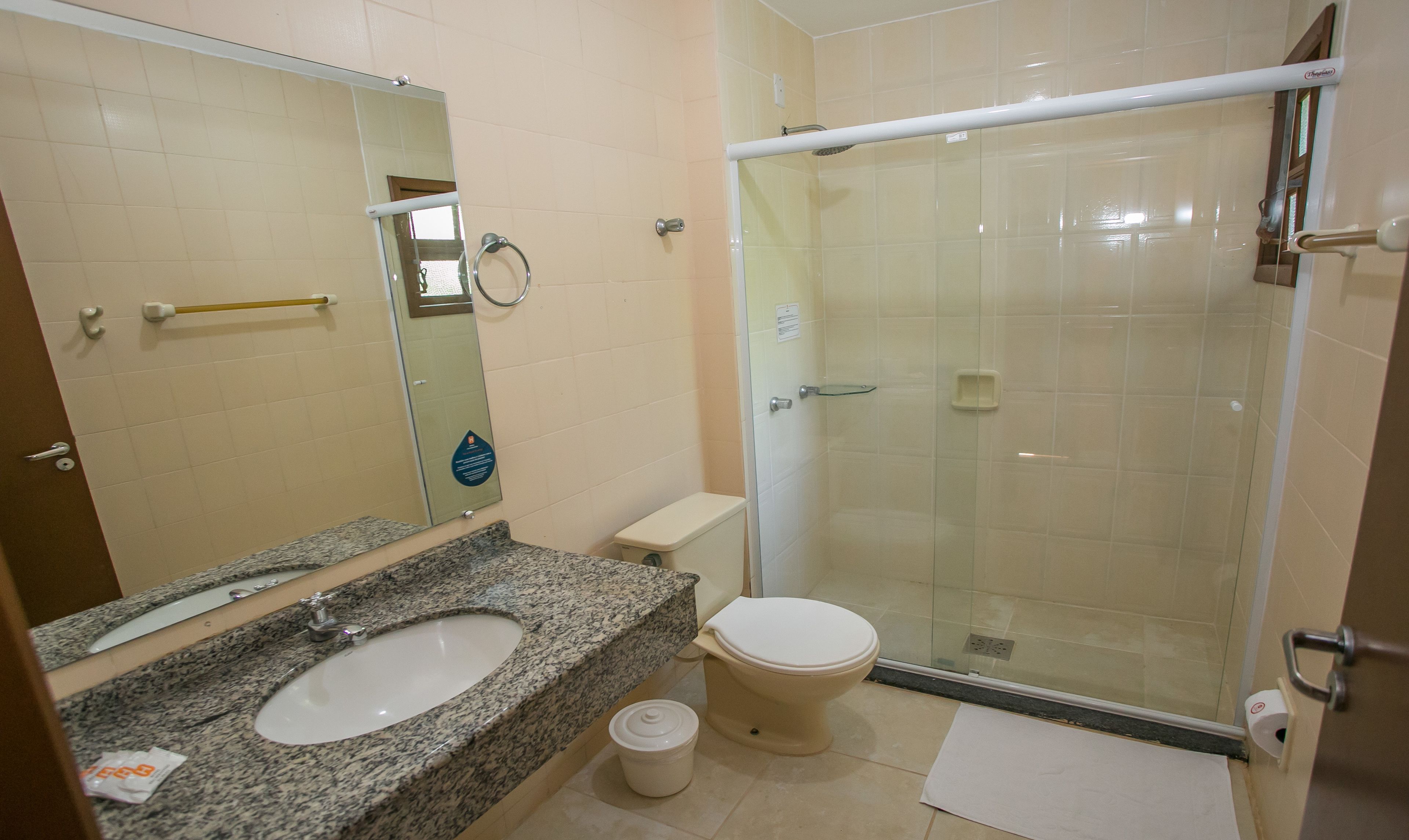 Un baño con lavamanos de encimera de granito, inodoro y ducha con mampara de vidrio.