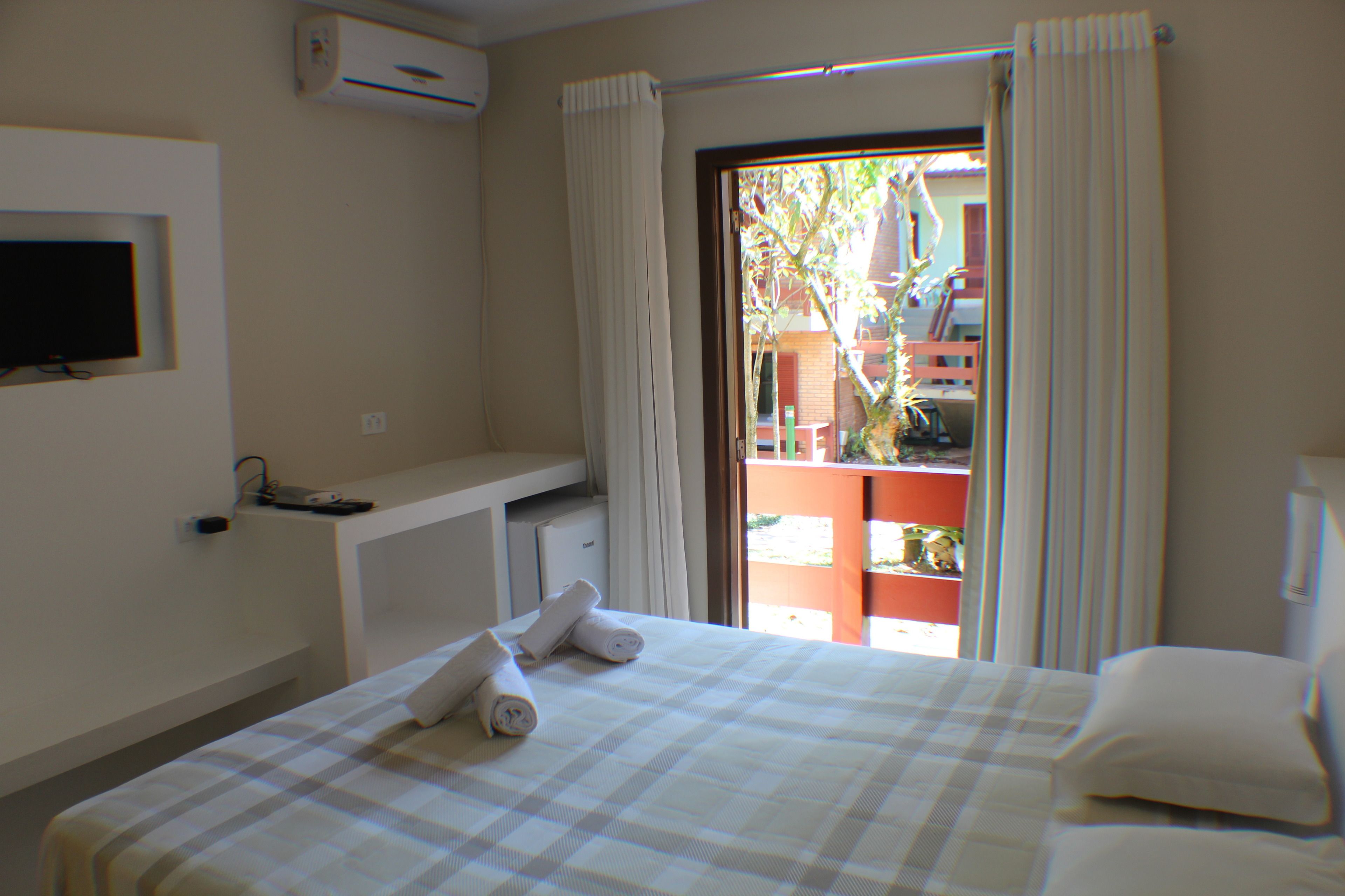 A hotel room with a bed, a TV mounted on the wall, a desk with a chair, and a view of the outside balcony.