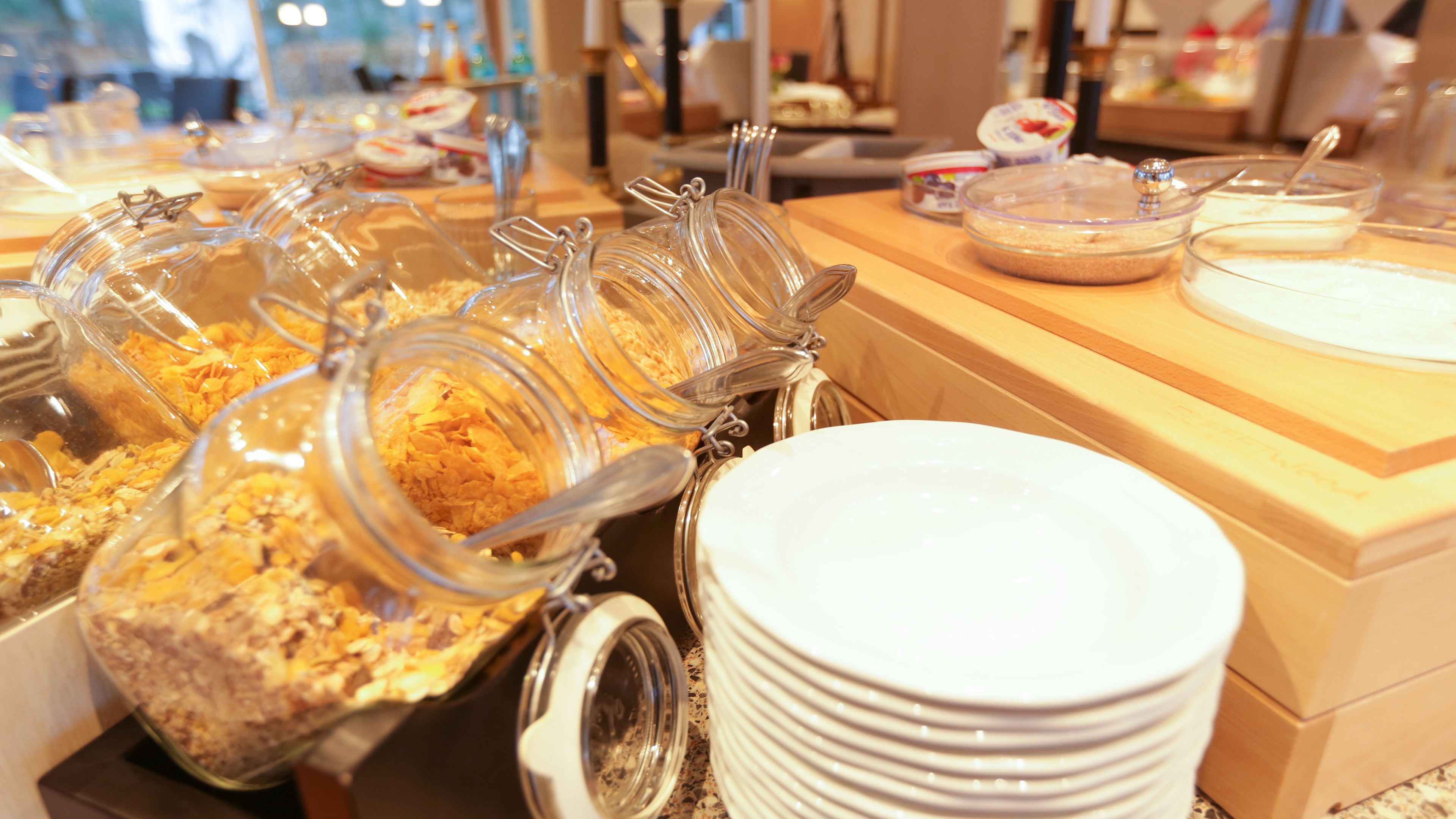 A buffet setup with various food items in clear containers, white plates, and a wooden counter.