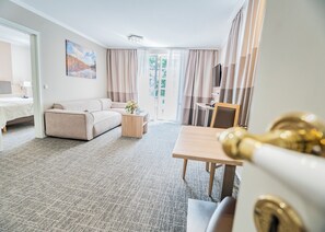 Habitación de hotel con sofá, una mesita con un jarrón, televisor y puerta con pomo dorado.