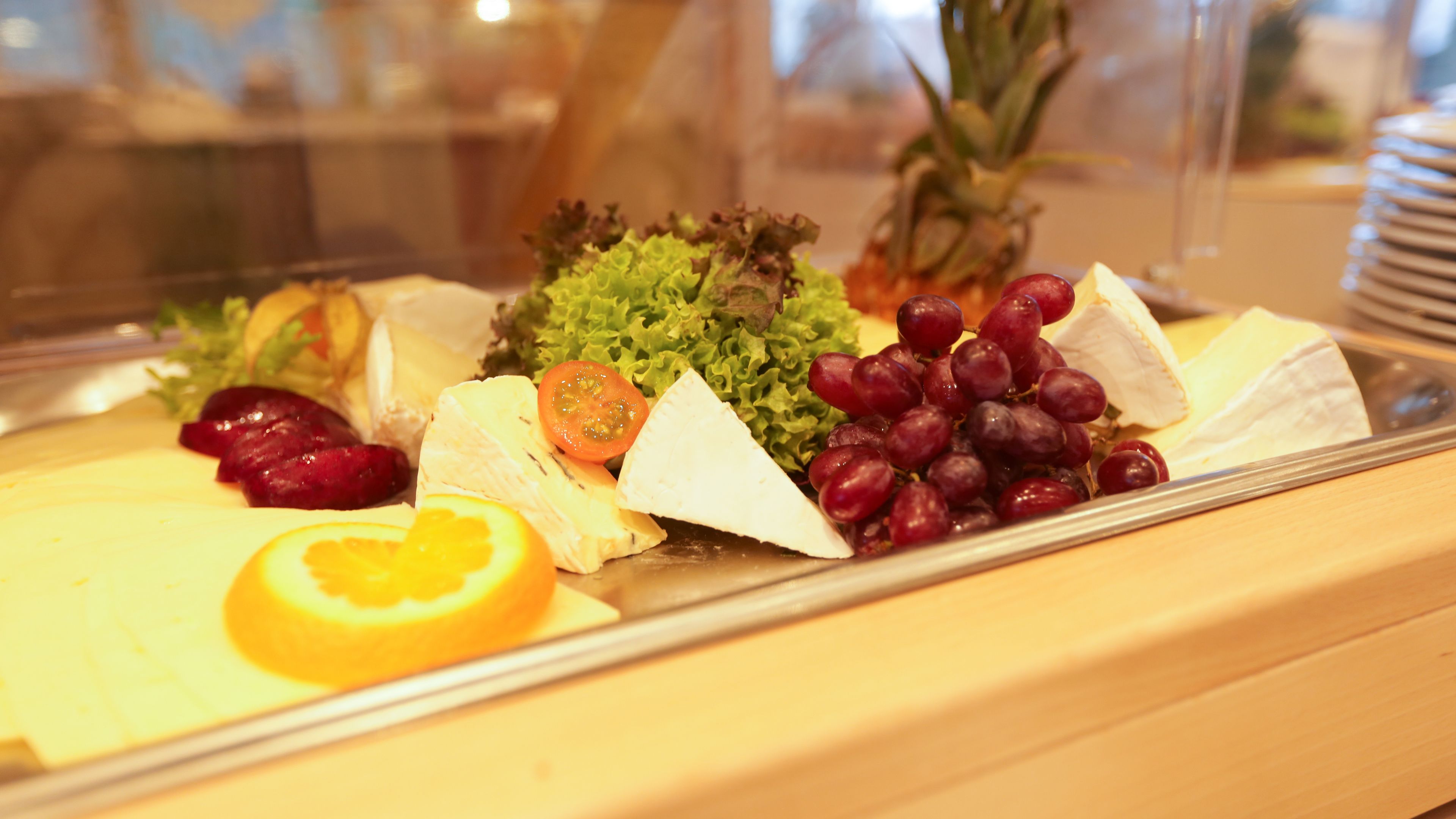 A cheese platter with various cheeses, grapes, and a slice of orange.