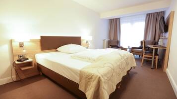 A hotel room with a large bed, bedside tables, a desk, and a chair.