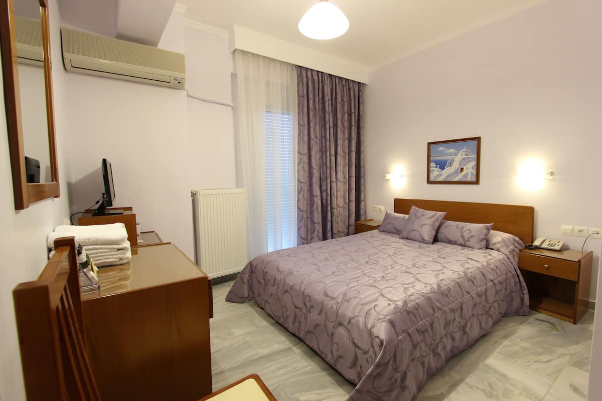 A hotel room with a bed, a desk, a chair, a bedside table, and a nightstand.