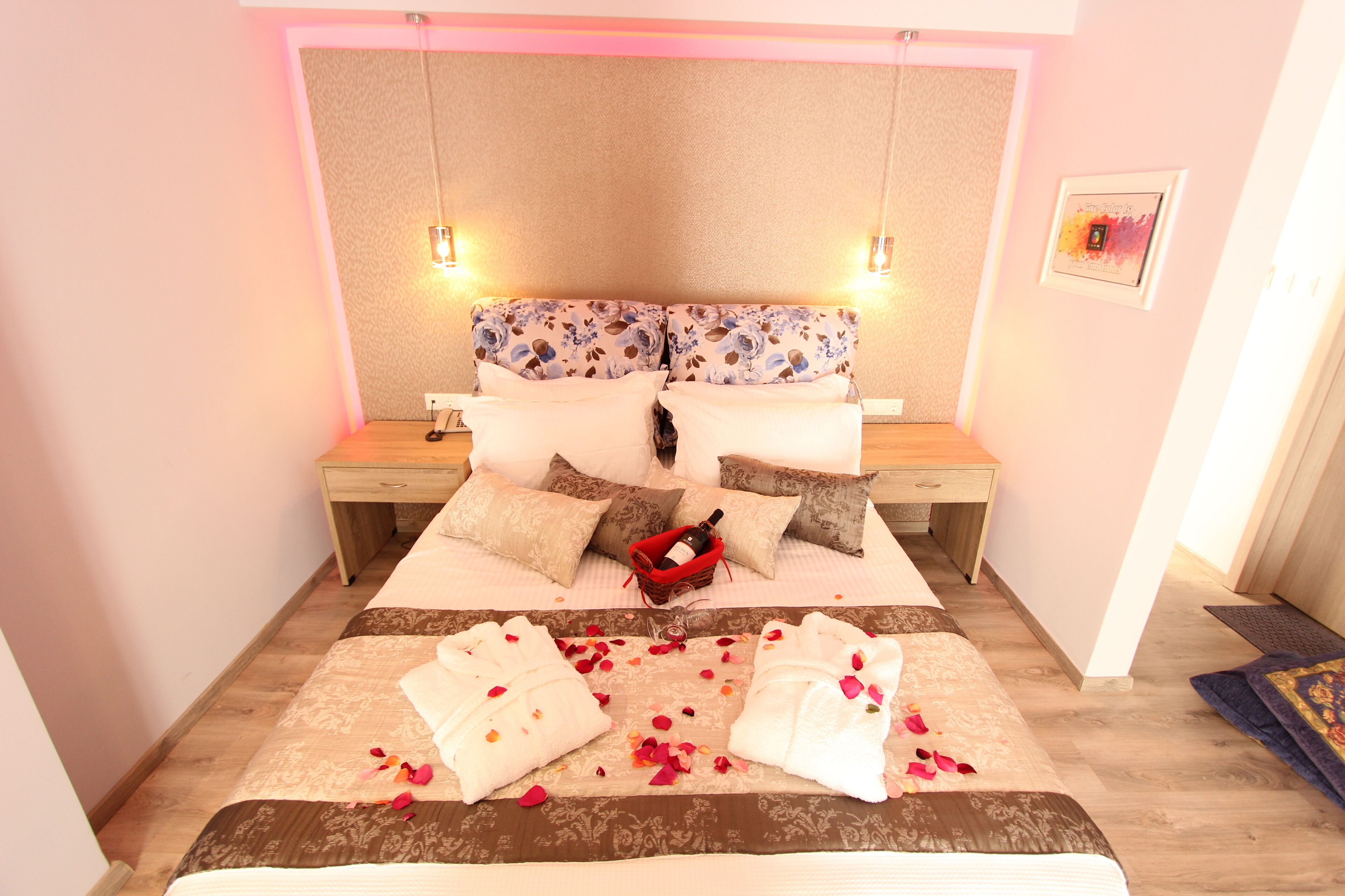 A neatly arranged bedroom with a bed, two bedside tables, a nightstand, a red basket with a bottle, and a framed picture on the wall.