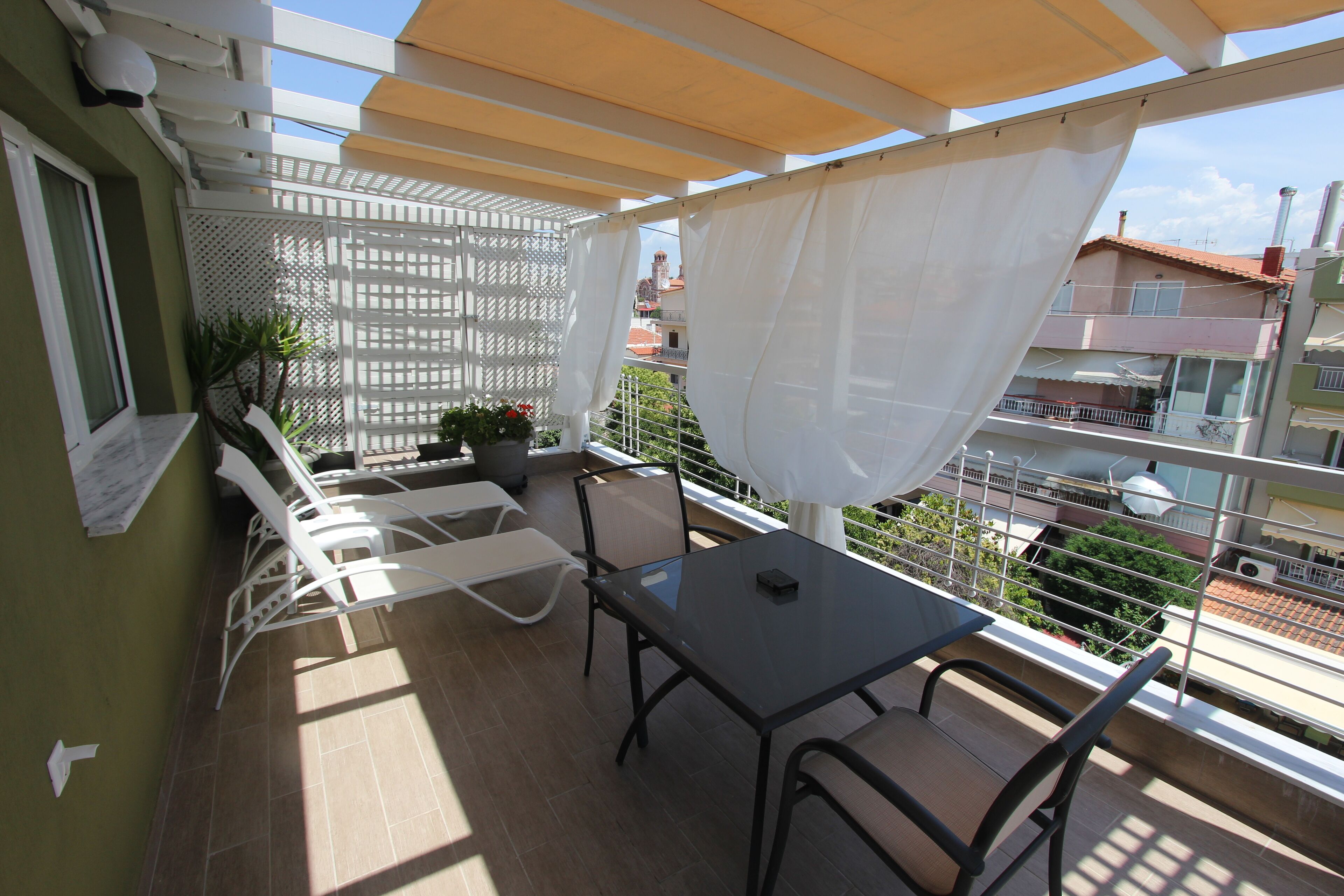 Un balcon avec une table et des chaises, une plante en pot et un rideau blanc.