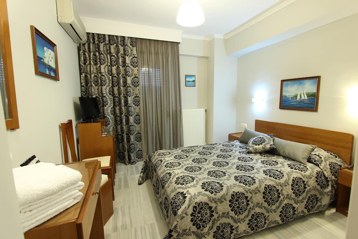 A hotel room with a bed, a desk, a chair, a TV, and a window with curtains.