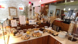A buffet counter with various food items, a coffee machine, and a mirror reflecting the room. - Hotel Mallas (Nea Propontida)