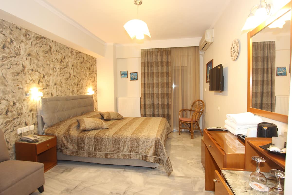 A hotel room with a bed, a chair, a desk with a mirror, and a clock on the wall.