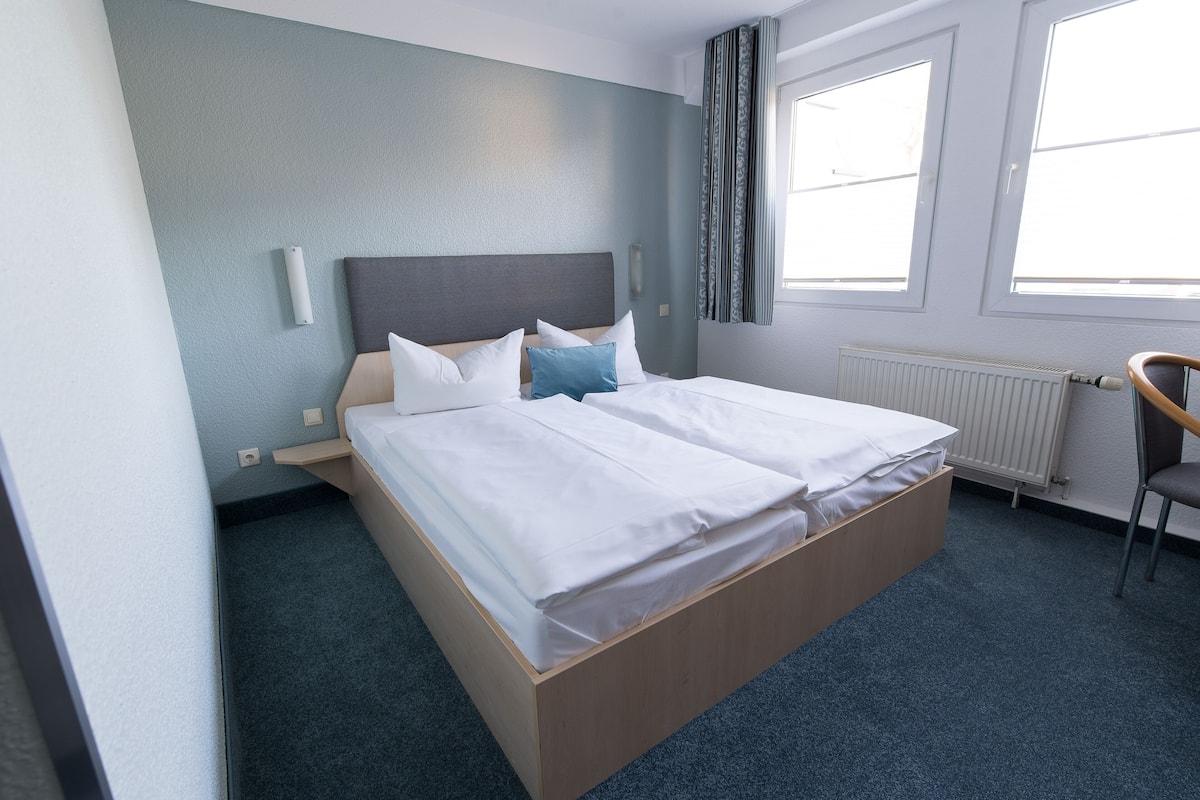 A hotel room with a bed, a chair, a window, and a radiator.