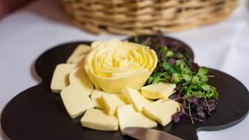 Un plato negro con un arreglo central en forma de flor hecho de queso amarillo, rodeado de trozos más pequeños de queso y una guarnición de hojas verdes.