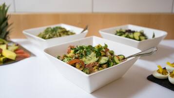 Three white bowls of salad with a spoon in each, placed on a white table.