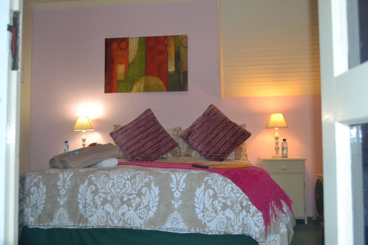 Una cama bien hecha con un edredón estampado, dos almohadas y una manta. Hay dos mesitas de noche con lámparas y una obra de arte en la pared sobre la cama.