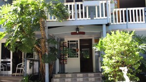 A two-story building with a balcony, a door with a sign, and a small garden area with plants.