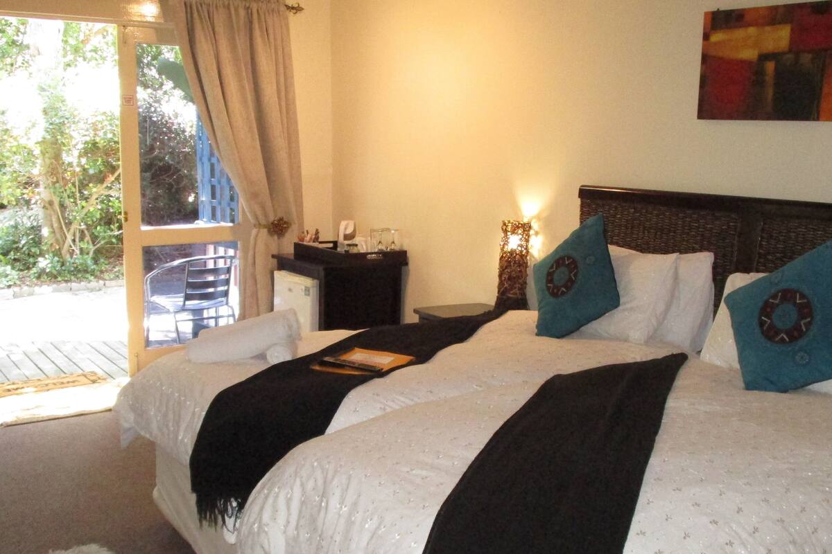 Un dormitorio con cama, mesita de noche, lámpara y vistas al exterior.