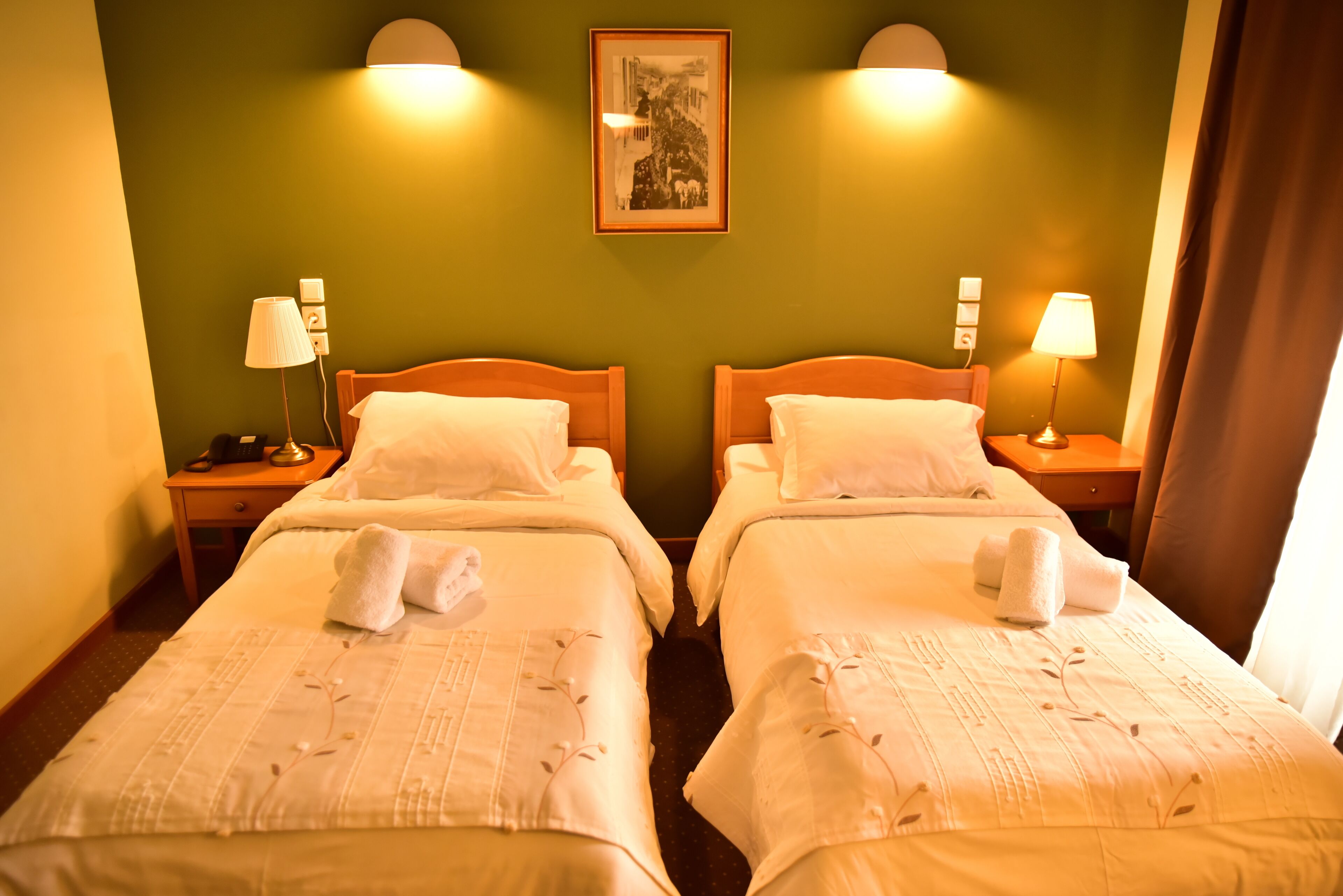 A hotel room with two beds, each with a pillow and a towel, a nightstand with a lamp, and a framed picture on the wall.