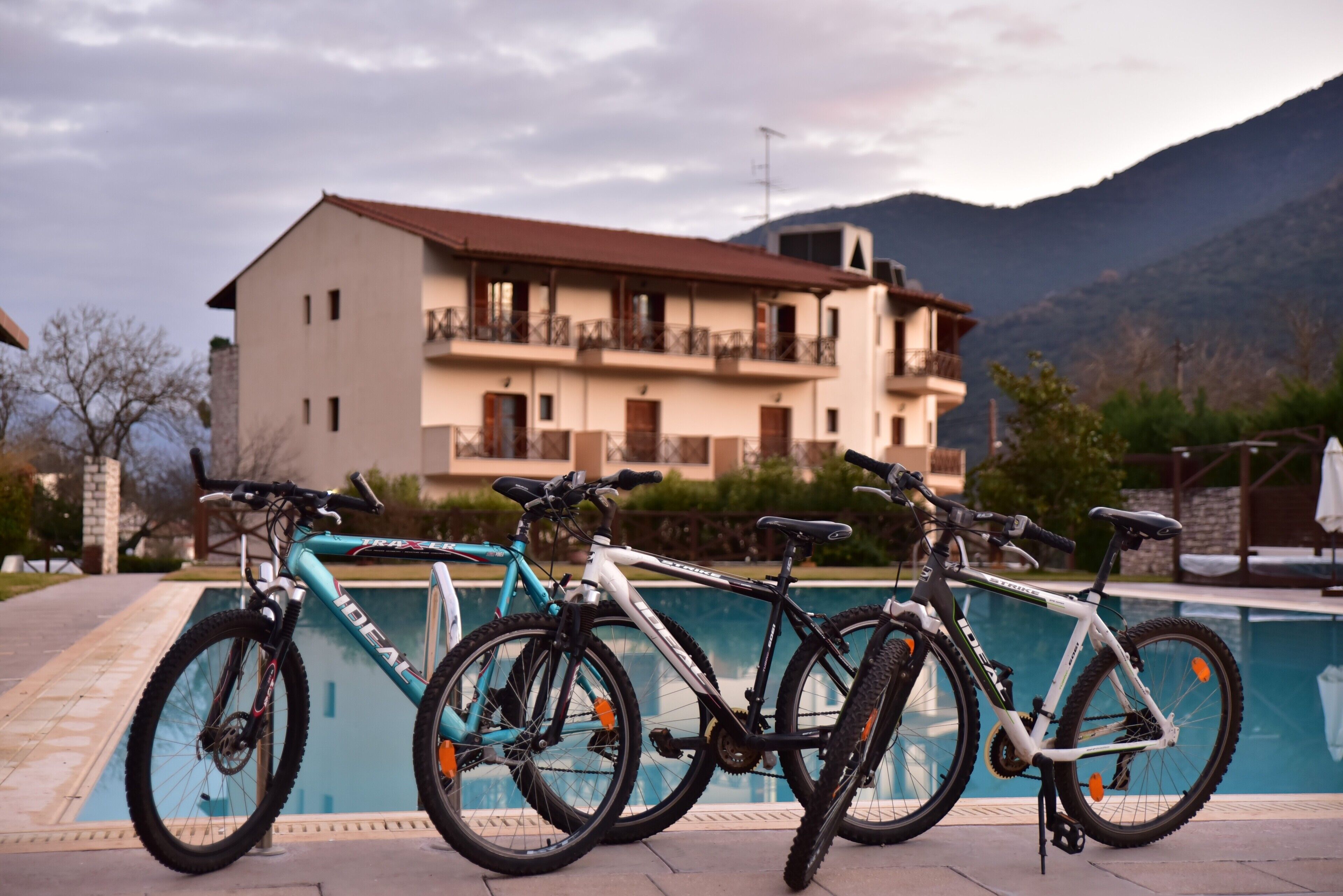 A poolside area with bicycles parked near a building with balconies and a mountain backdrop.