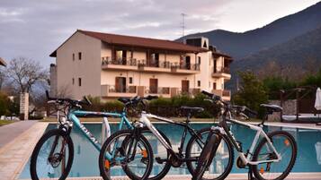 A poolside area with bicycles parked near a building with balconies and a mountain backdrop.