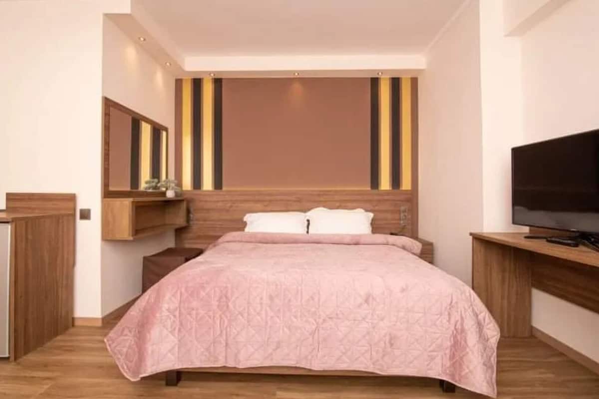 A modern hotel room with a large bed, a TV, and a wooden headboard.