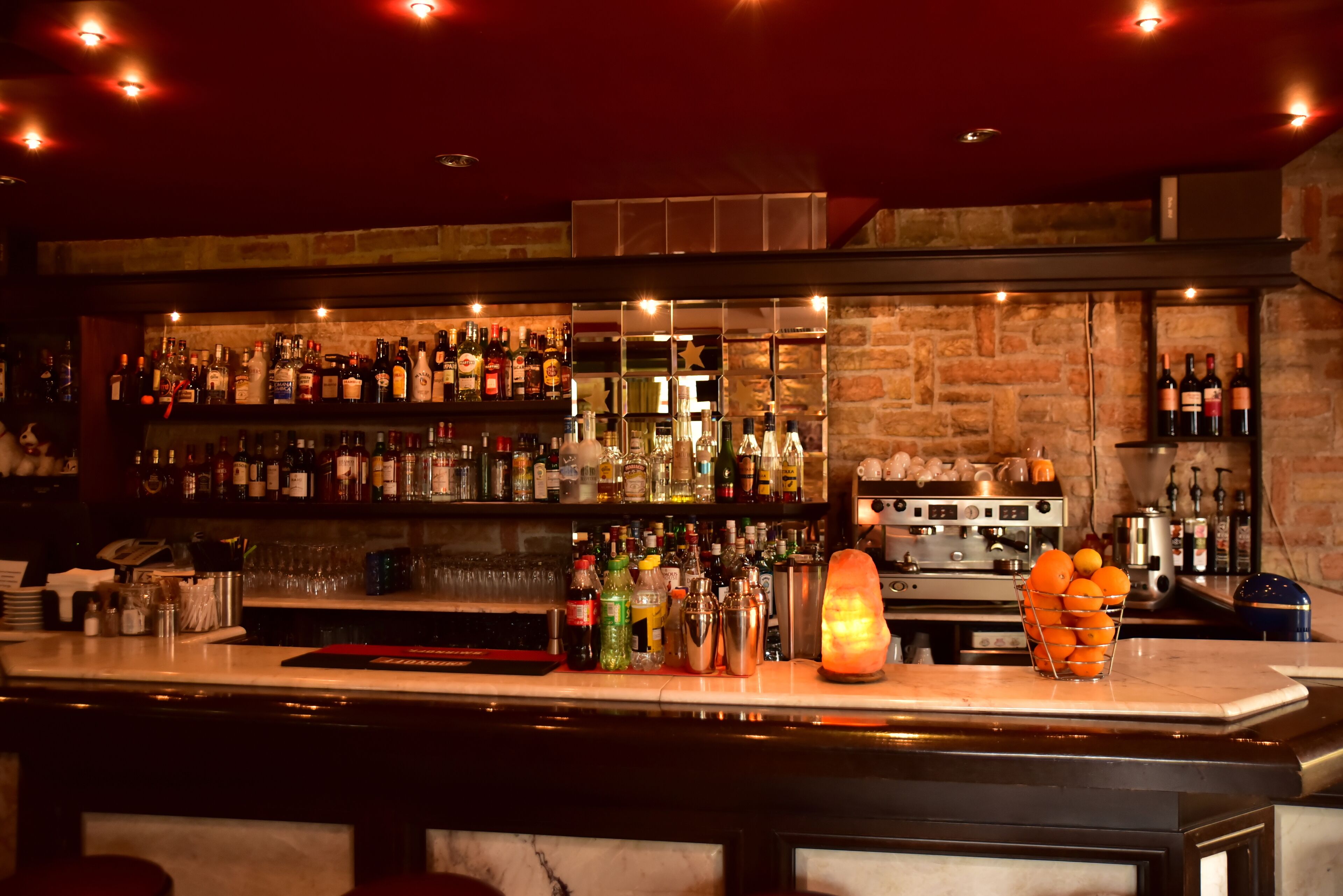 A bar area with shelves of liquor bottles, a cocktail shaker, and a fruit basket.