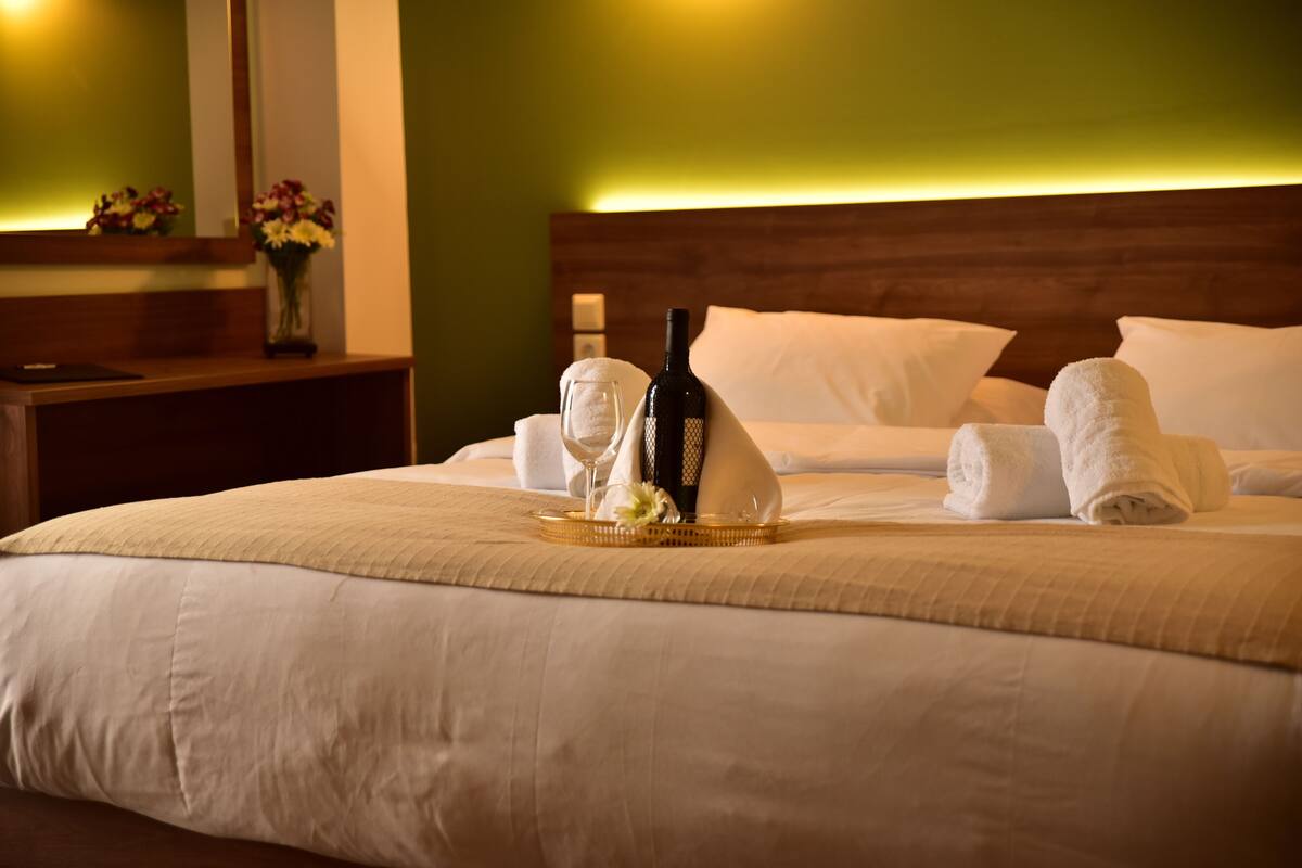 A neatly made bed with a bottle of wine, a glass, and a tray of flowers.