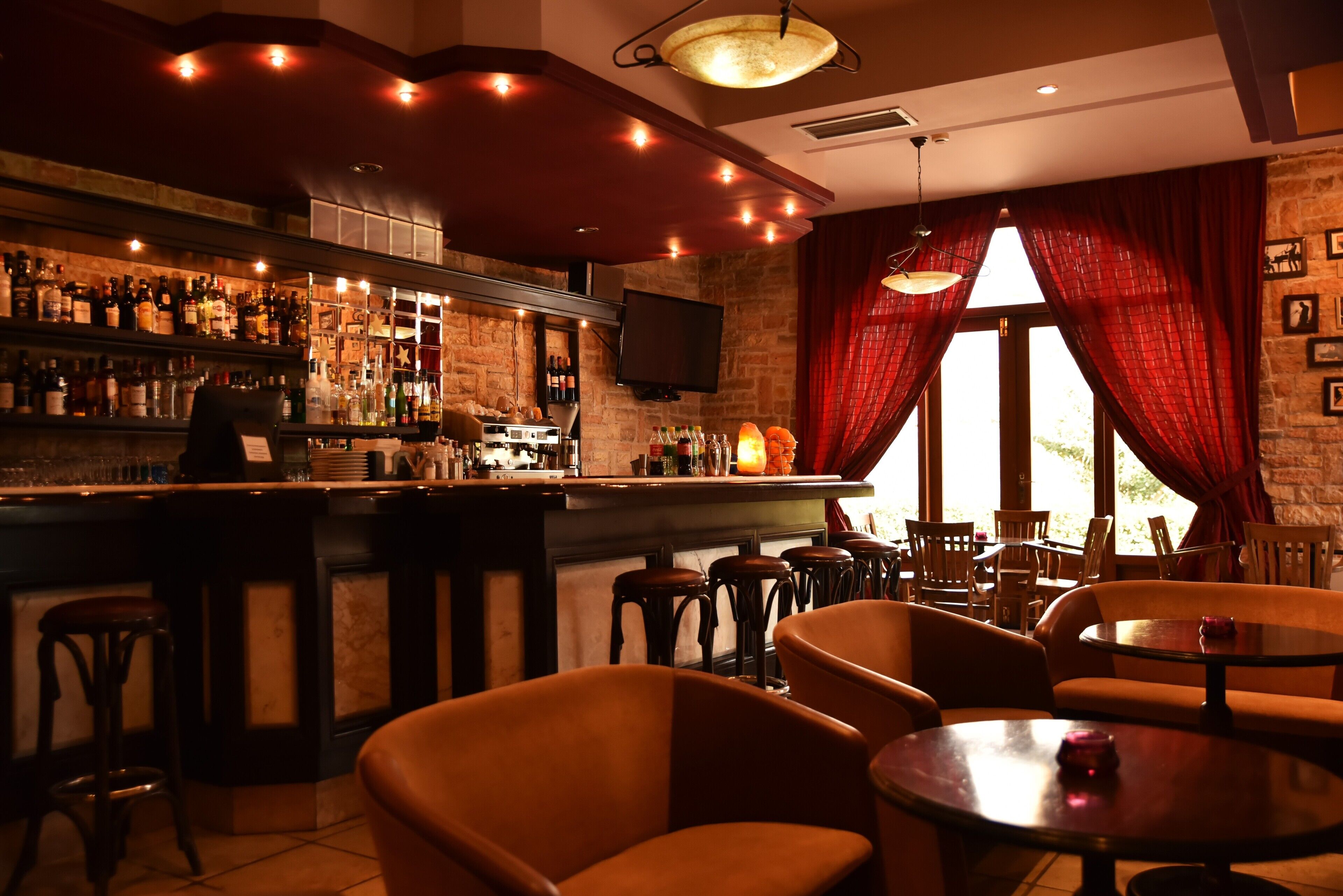 Un espace bar comprenant un comptoir, des tabourets et un coin salon avec des tables et des chaises.