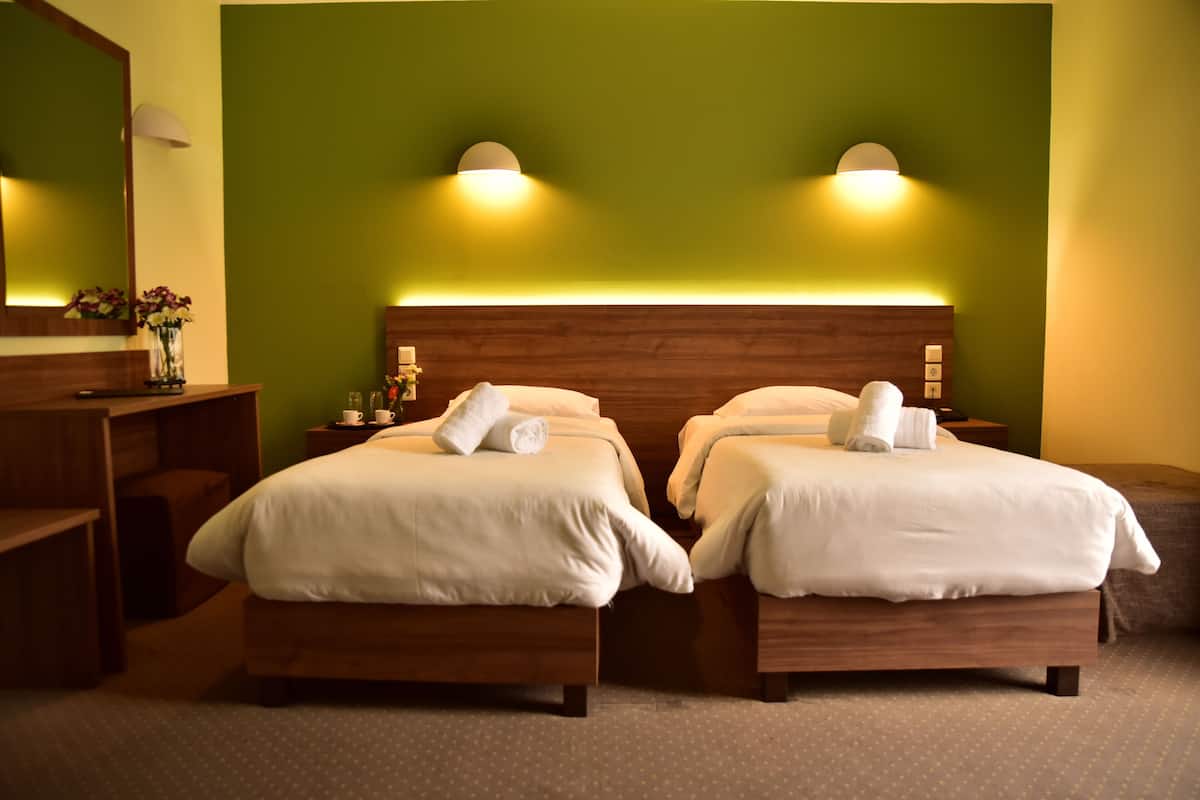 A hotel room with two beds, a wooden headboard, a nightstand with a lamp, and a mirror.