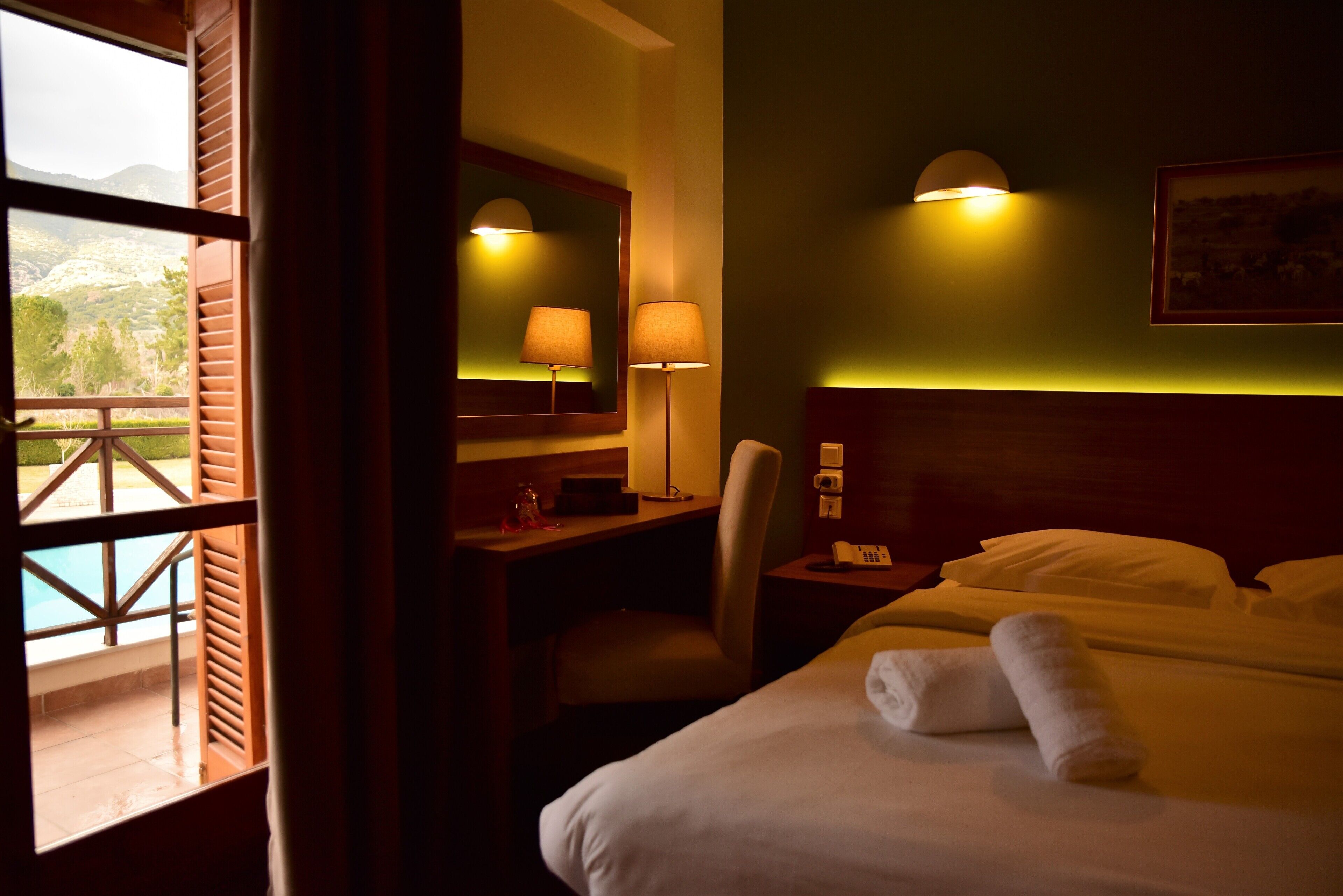 A hotel room with a bed, a desk, a chair, a telephone, and a window with a view of the outdoors.