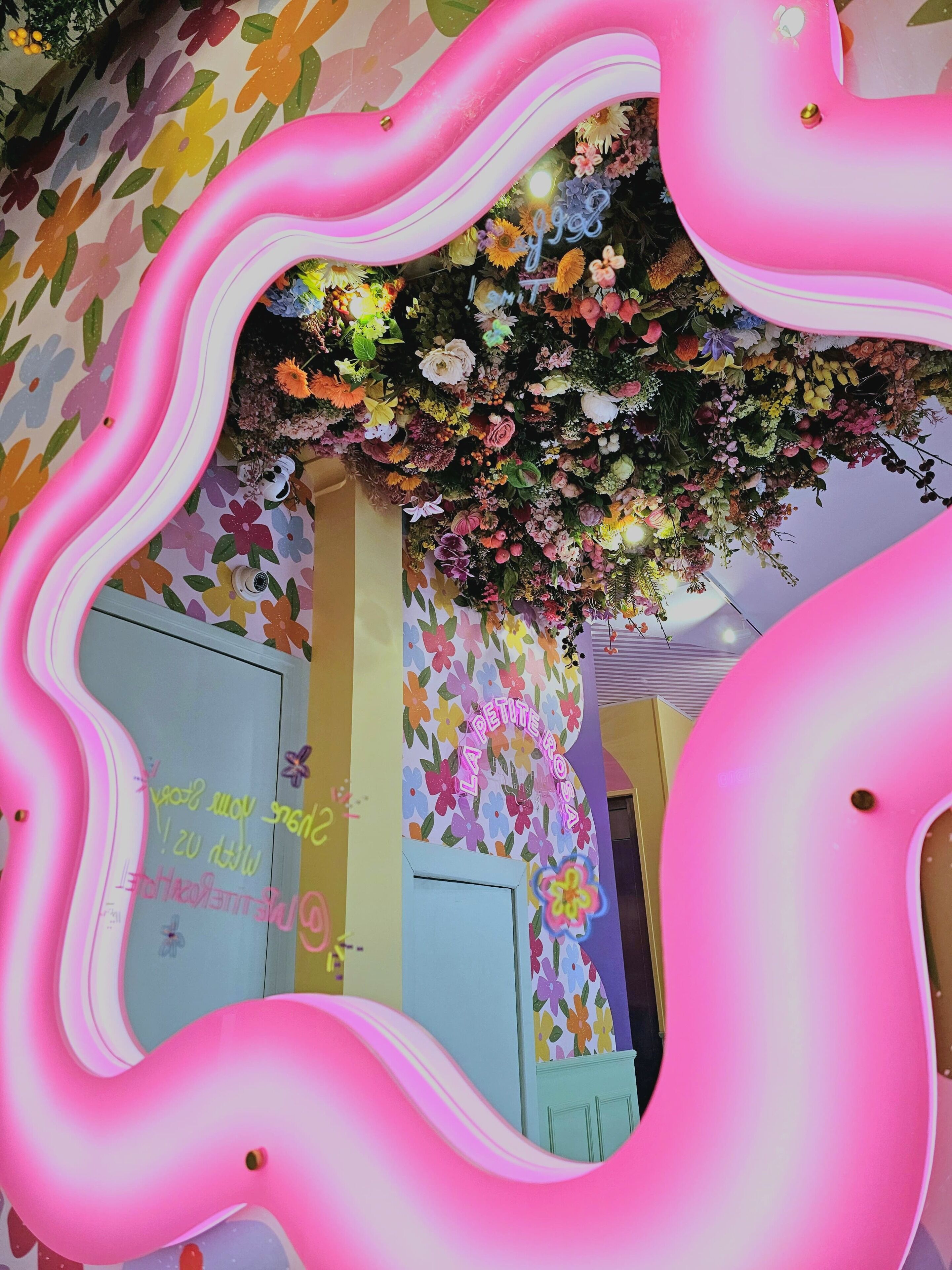 A room with a pink wavy mirror, floral wallpaper, and a door with a sign.