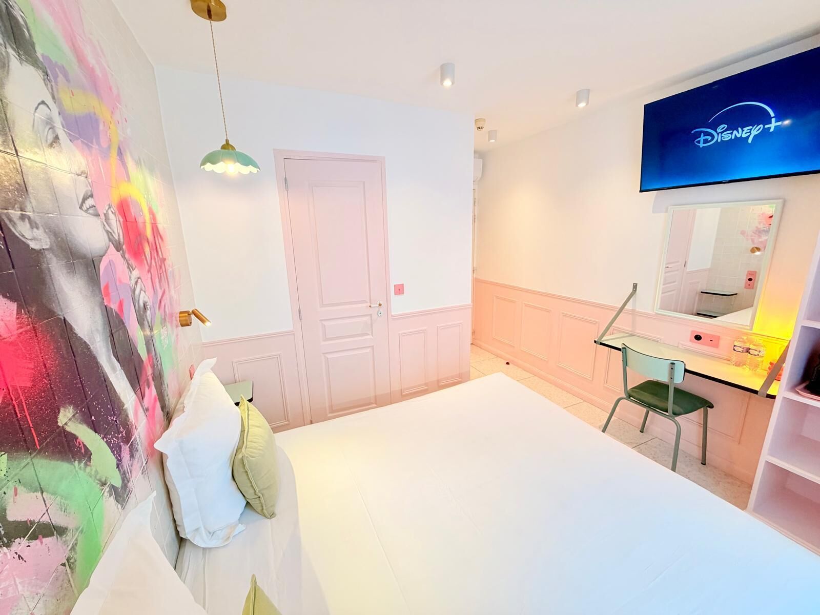 A bedroom with a bed, a dresser, a mirror, a TV, and a colorful wall mural.