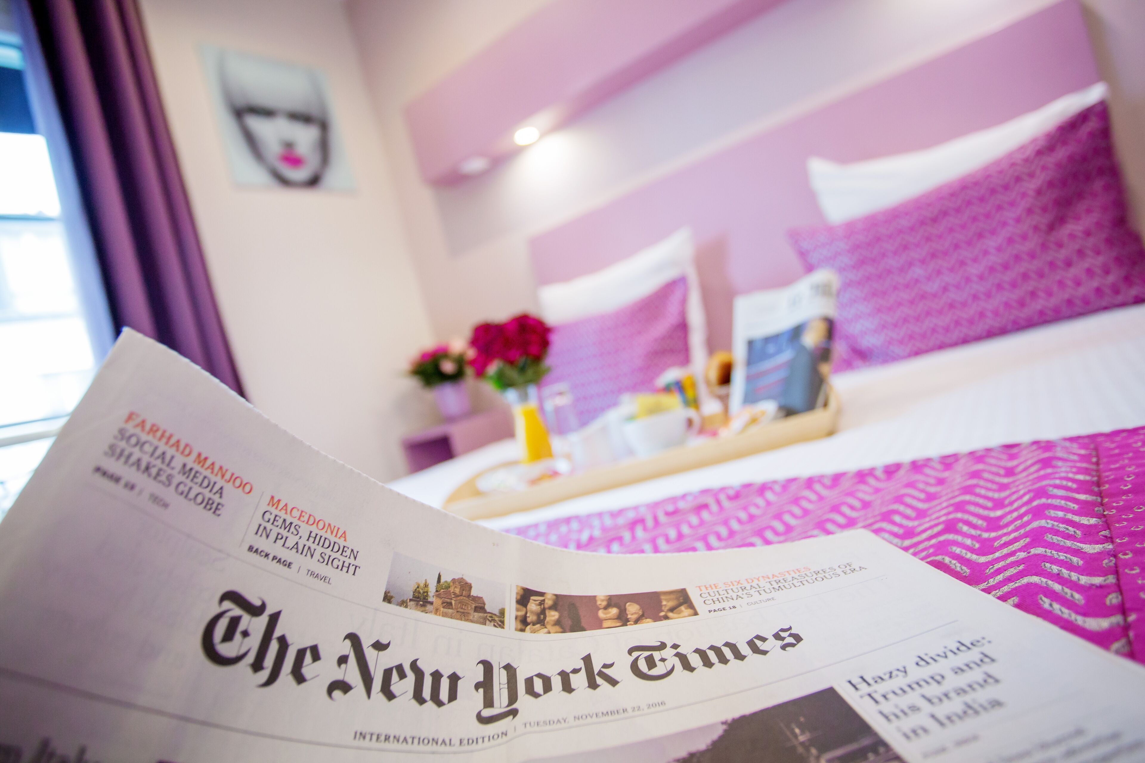 A hotel room with a bed, a bedside table, and a newspaper on the bed.