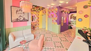 Een levendige hotellobby met een geruit vloertje, een kroonluchter, een bank en een spiegel.