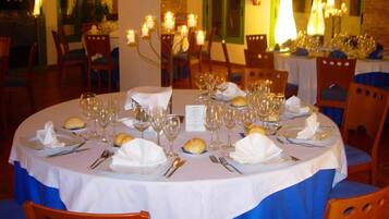 Une table de salle à manger ronde, recouverte de nappes blanches, avec de nombreux verres à vin, ainsi que des assiettes et des couverts disposés avec soin.