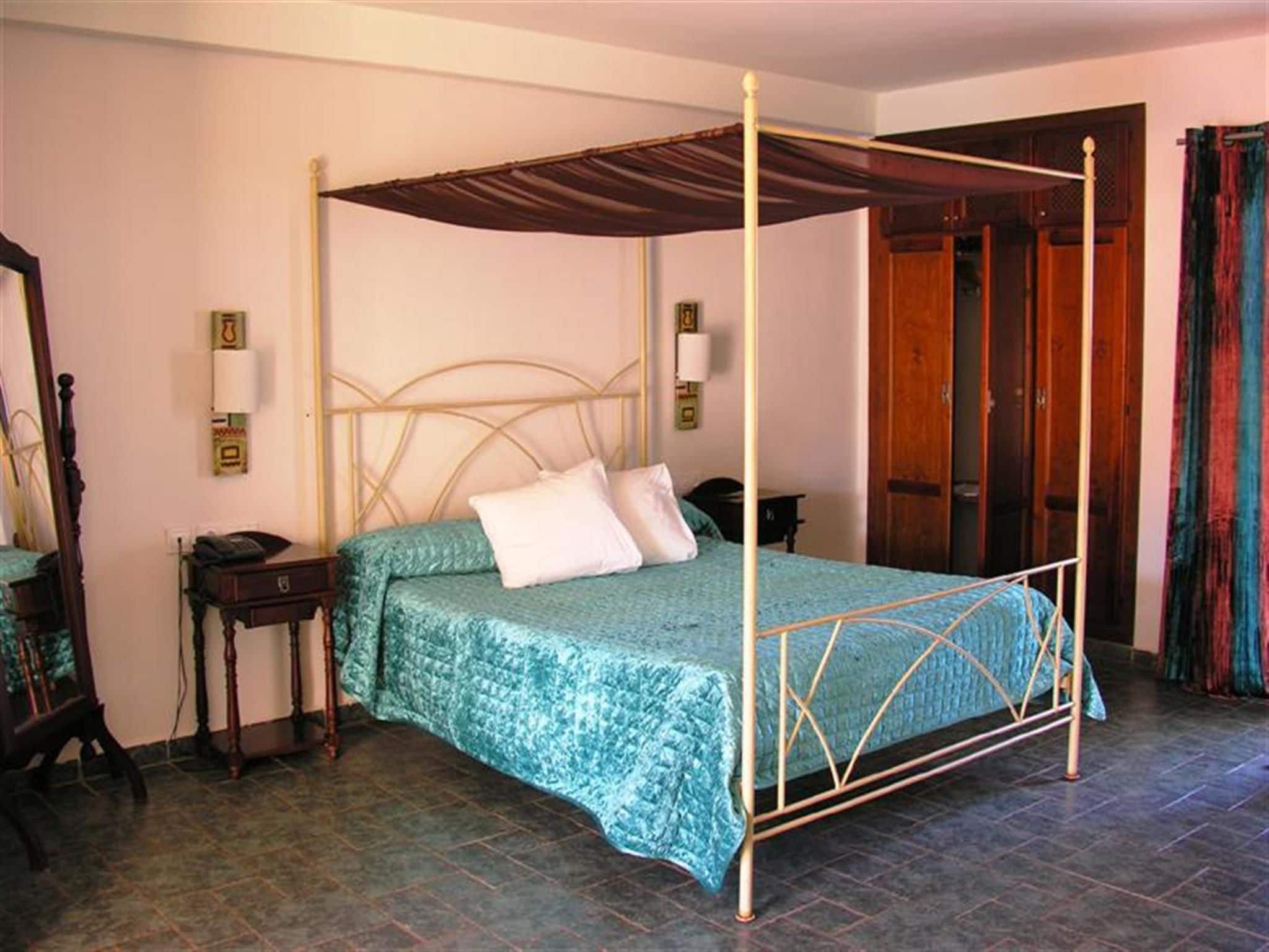 A four-poster bed with a canopy, a bedside table, a nightstand, and a mirror.