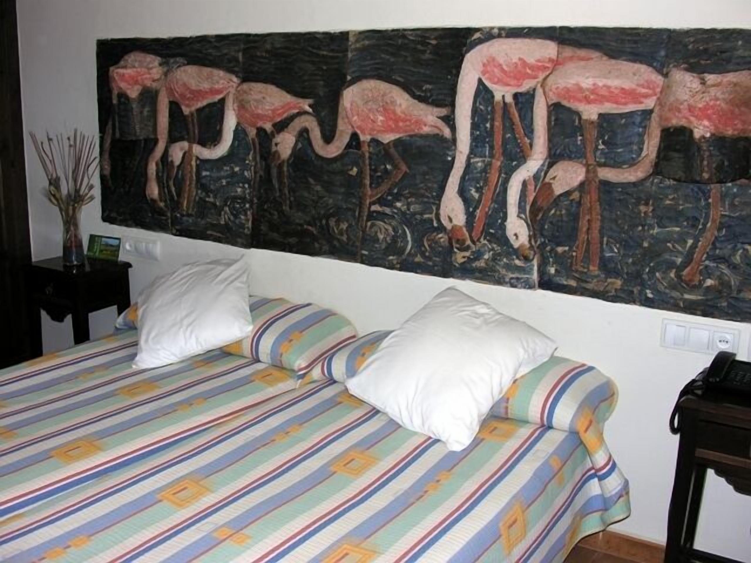 A hotel room with a large bed, two pillows, a nightstand, and a painting of flamingos on the wall.