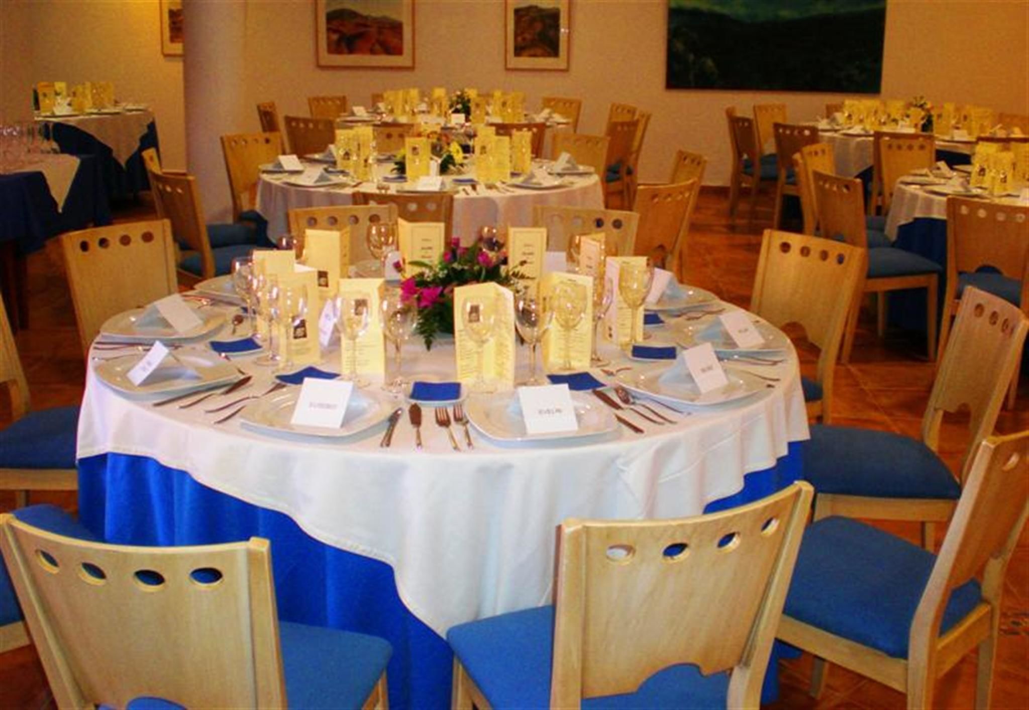 A round dining table set for a formal event with name cards, place settings, and a centerpiece.