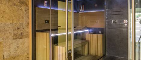 A sauna with glass walls, wooden benches, and a metal floor.