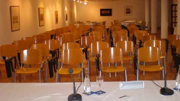 Un salón de conferencias con filas de sillas, una mesa blanca con un micrófono y una placa de identificación.