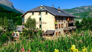 A building with the sign 'arachin' on the side, surrounded by a field of flowers and mountains in the background. - Le Faranchin (Villar-d'Arene)